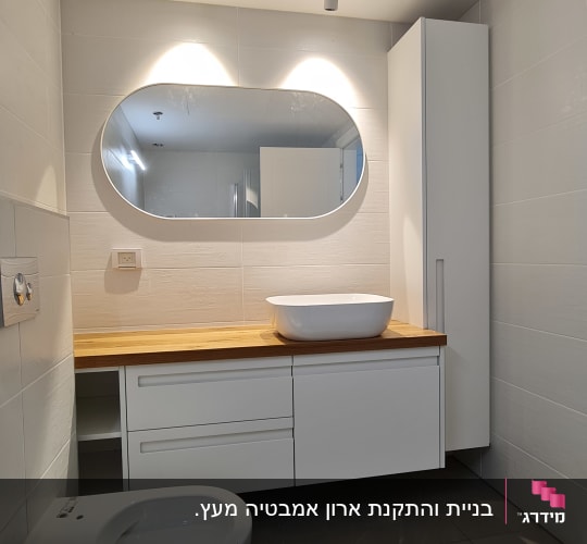 חדר אמבטיה עם כיור על משטח עץ ומראה אובלית
